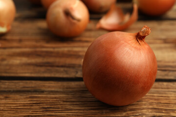 Ripe onion bulbs on wooden table. Space for text