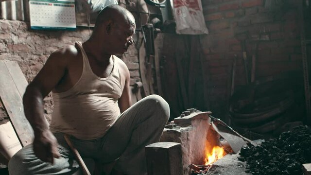 Rural blacksmith placing a metal piece in a furnace hot fire
