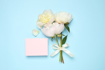 Obraz na płótnie Canvas Beautiful bouquet of fresh peonies and blank card on light blue background, flat lay. Space for text
