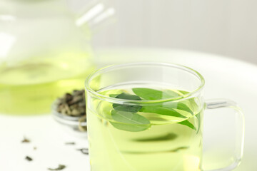 Cup of aromatic green tea with leaves on light background, closeup