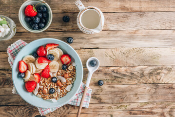 Healthy breakfast bowl with oat granola with dried buckwheat, nuts and coconut chips, berries and rice milk