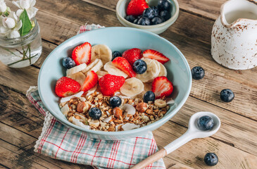 Healthy breakfast bowl with oat granola with dried buckwheat, nuts and coconut chips, berries and rice milk