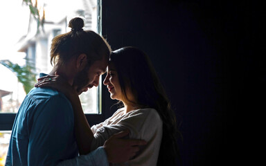 Smiling Caucasian man husband embracing his beautiful pregnant wife and looking her face with love. Couple have romantic moment together. Family bonding relationship and maternity healthcare concept.