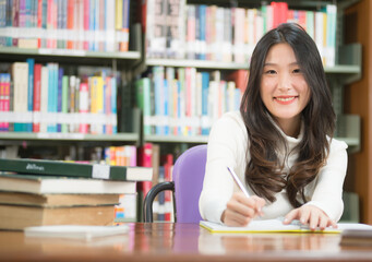 Asian women do homework in the library. Her face is smiling