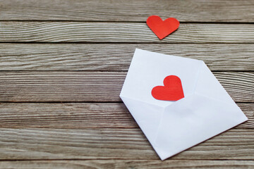 two red paper hearts on white open envelope against gray wooden background