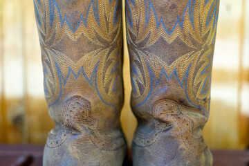 Old brown leather cowboy boots decorated with stitching in yellow and blue thread.