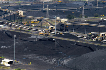network of conveyor belts over coal terminal heaps with bulldozers and trains in the background....