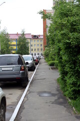 There are cars in the parking lot in the courtyard of the house next to the footpath