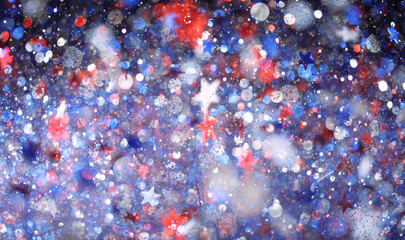 Background of red, white, and blue sparkling glitter scattered with shiny stars confetti. 4th of...