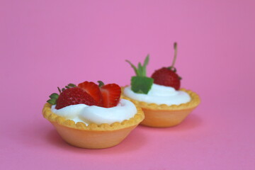 Two tartlets with cream and strawberries on a pink background