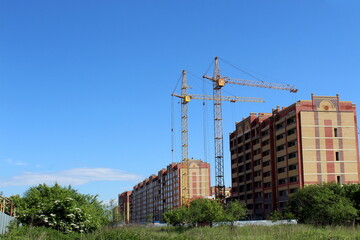 Fototapeta na wymiar Two cranes build a house on the outskirts of the city on a summer day