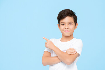 Close-up portrait of smiling young boy pointing finger on blank space beside in blue isolated background