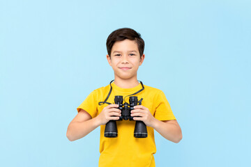 Portrait of smiling young boy holding binocular while looking at the camera in isolated studio blue background © Atstock Productions