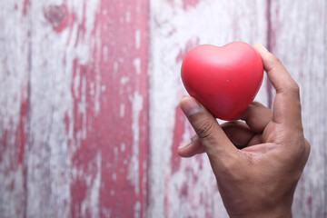 Man holding red heart in hands on wooden table .