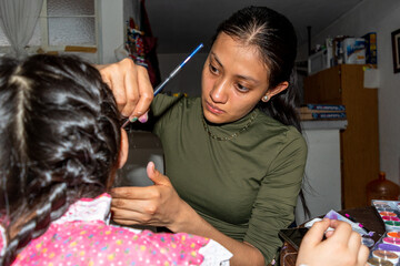 Young woman putting makeup of Catrina in a girl's face