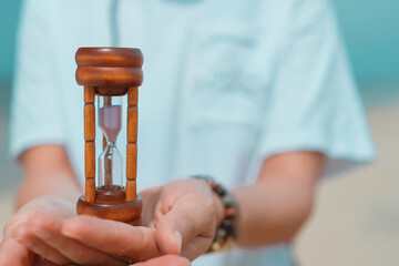 Hand hold small hourglass model show time is flowing on summer beach.
