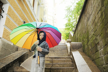 cute preschooler in a transparent protective water-repellent raincoat holds a rainbow umbrella...