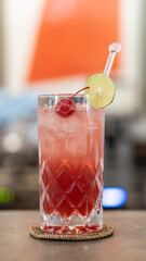 Cocktail with a beautiful red color in a glass with lemon and cherry against a blurred background.