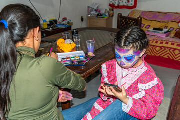 Young woman putting makeup of Catrina in a girl's face