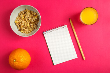 cup of granola and fruits and a notebook for writing calories on a pink background.