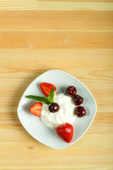 Ice cream dessert with strawberries and cherries in a plate on a wooden table. Copy space.