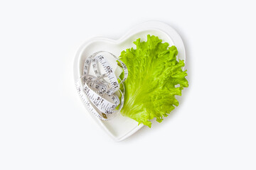 Weight loss diet. Fresh green leaf lettuce and measuring tape on heart shaped plate on white background. Healthy eating. Organic and vegetarian food. Flat lay, copy space for text