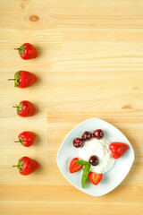 Ice cream dessert with strawberries and cherries in a plate on a wooden table. Copy space.