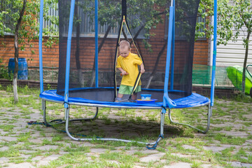 A little boy in a yellow T-shirt jumps on a big trampoline in the garden
