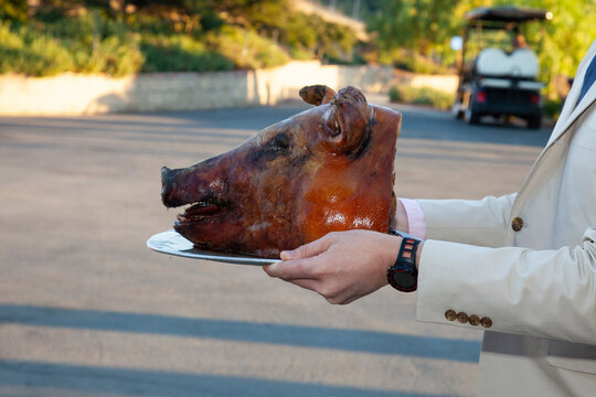 Roasted pig's head being served on a silver platter outside by a person