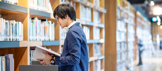 Asian man university student reading book by bookshelf in college library for education research....