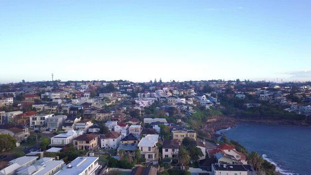 Rise up aerial view of residential houses with ocean view in the neighborhood revealing Sydney city skyline