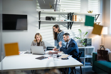 In Creative Office Productive Coworkers Standing at the Table, Company Meeting. Colleagues and clients talking strategy with laptop and tablet.