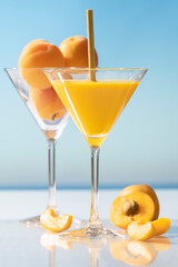 martini glass with apricot juice and a straw surrounded by an open apricot and some slices
