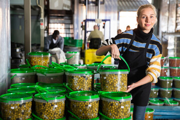 Female worker stocks plastic containers and cans with olives in warehouse