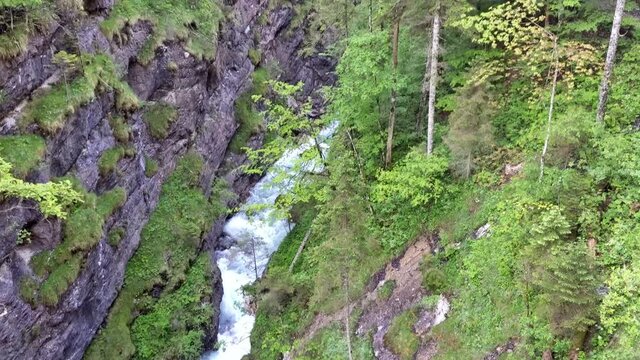 Aerial view of mountain river Partnach forcefully flowing through the canyon. 
Camera tilt upwards along the canyon to the high mountains and blue sky in the background.