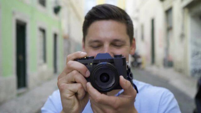 Happy young man taking pictures in old city street, working with dslr photo camera. Front view, closeup shot. Photographer concept