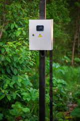 The electric box is hanging on a pole on the street.