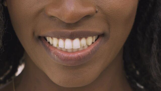 Lower face of young African American woman with dreads smiling at camera, posing, showing white teeth. Front view, closeup, cropped shot. Human emotions or dental care concept