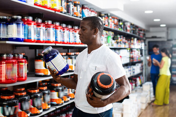 Fototapeta na wymiar Focused muscular African man choosing sports nutrition products in shop, reading content label