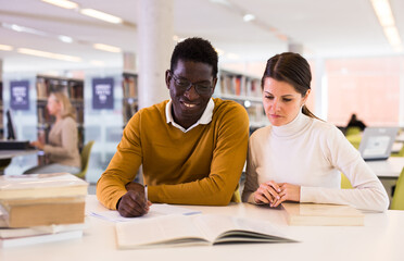 Portrait of couple of adult students studying together in public library