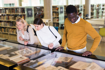 Professor and adult students read ancient books in a library showcase