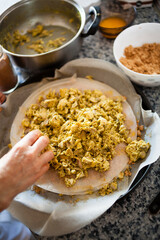 Vertical shot of a traditional moroccan pastilla under construction with a woman hands spreading the cooked spiced chicken and ingredients on the background. Morocco typical dishes preparation.