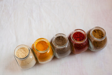 Five seasoning spices on powder to your meals: ginger, curcuma, cumin, paprika and black pepper on a white linens background. Moroccan and asian food flavor stills with negative space.