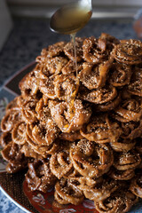 Vertical shot of a big size plate full of freshly fryed chebakia Moroccan sweets with a spoon topping the biscuits with a mix of honey and orange flower water. Ramadan food vertical stills.