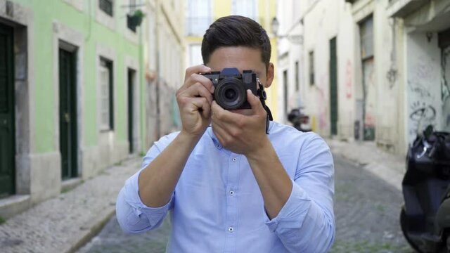 Focused young man taking pictures in old city street, holding and using dslr photo camera. Front view, medium shot. Photographer concept
