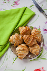 Vertical shot of homemade french croissants on a traditional plate with a green napkin, vintage knife and floral soft tablecloth with copy space.