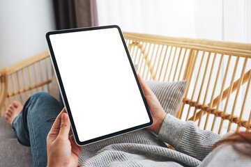 Mockup image of a woman holding black tablet pc with blank desktop white screen while lying on a...