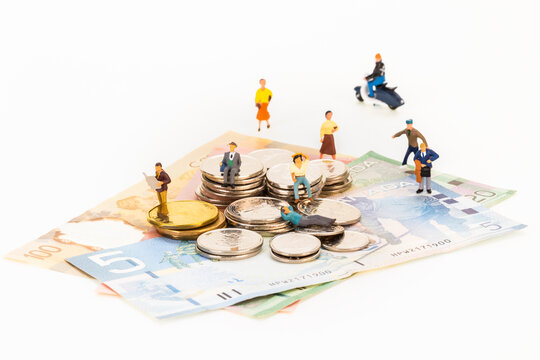 Miniature men and women on top of coins and banknotes over white background