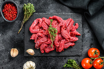 Raw meat cut into thin strips for beef Stroganoff. Black background. Top view