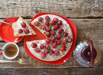 Confectionery background. Round pie with red strawberries on top on a red plate on a wooden natural background. Home cooking.